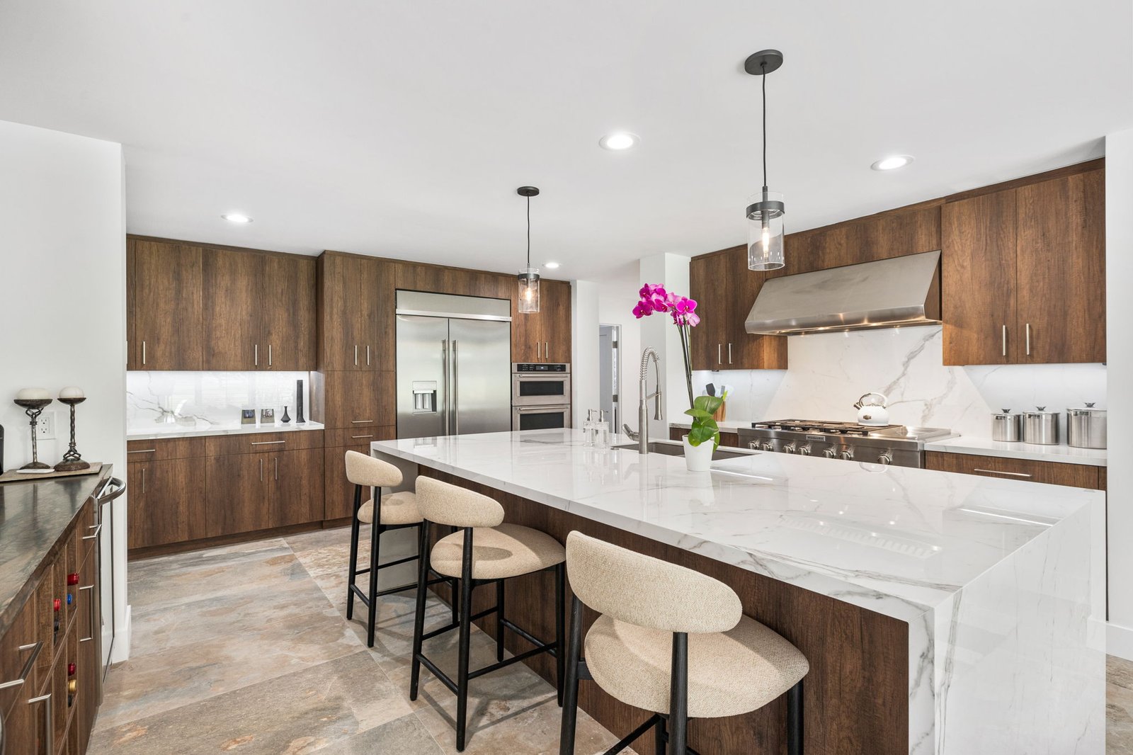 Sub-Zero refrigerator luxury kitchen with walnut cabinetry, marble island, and island seating